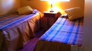 A small, cozy room with two single beds, a nightstand, and a window with a curtain. - Departamento Modulo Alto Mirasol 2 (Algarrobo)