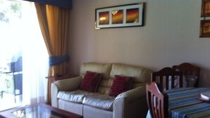 A living room with a leather sofa, a glass-top coffee table, a striped bed, and a framed picture on the wall. - Departamento Modulo Alto Mirasol 2 (Algarrobo)