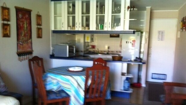 A compact kitchen with white cabinets, a small dining table with chairs, and a refrigerator. - Departamento Modulo Alto Mirasol 2 (Algarrobo)