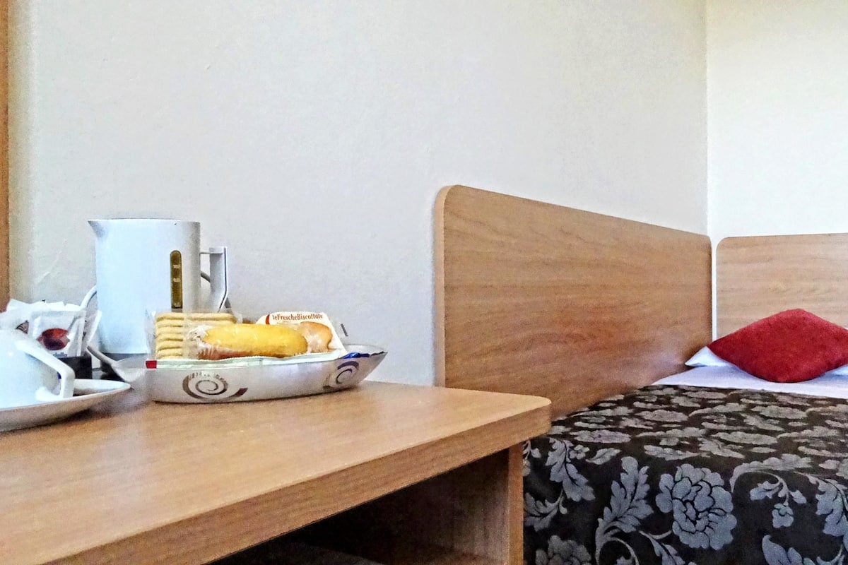 Une chambre d’hôtel avec un lit en bois, une table de chevet sur laquelle se trouve un plateau avec des articles pour le petit-déjeuner, et un tableau accroché au mur.