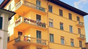 Un edificio amarillo de varios pisos con balcones, un coche estacionado en la calle y un cartel de prohibido estacionar.