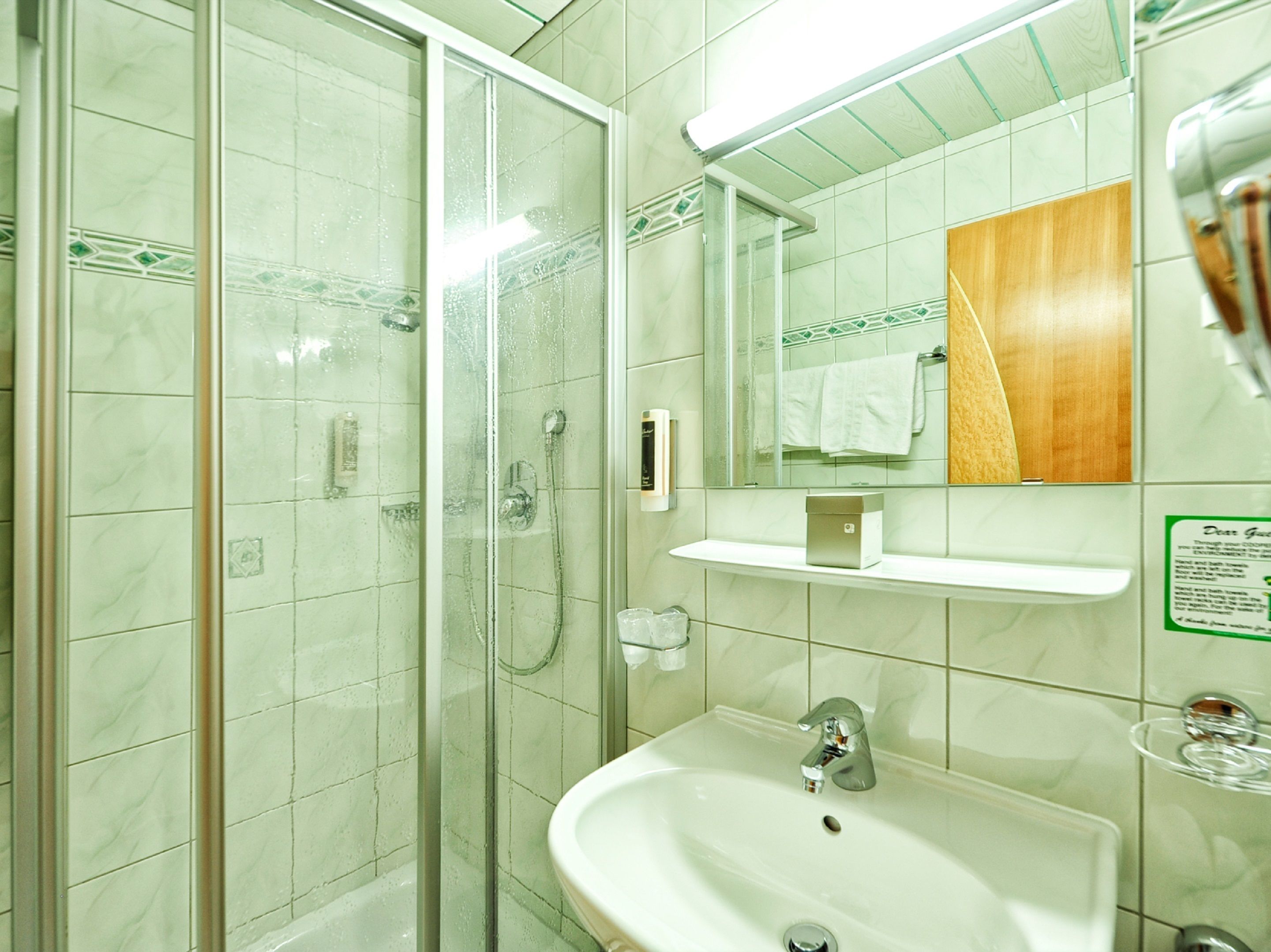 Un baño con ducha envuelta en vidrio, un lavamanos, un espejo y un perchero para toallas.