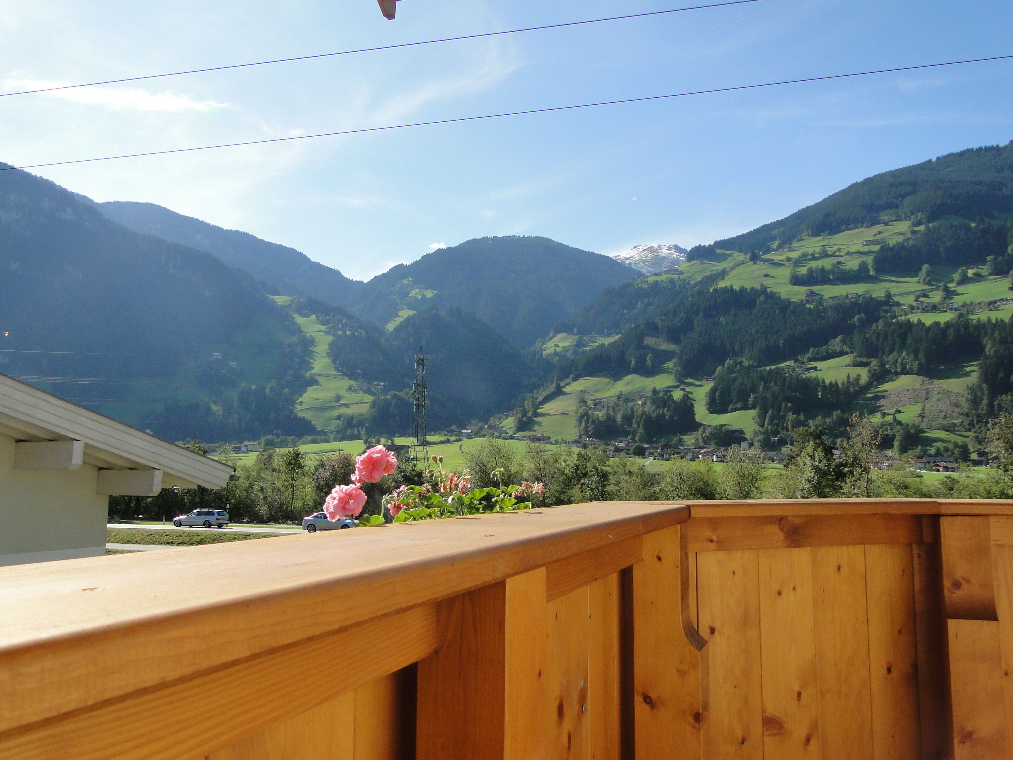 A wooden deck with a view of a mountainous landscape, including green fields and a snow-capped peak.