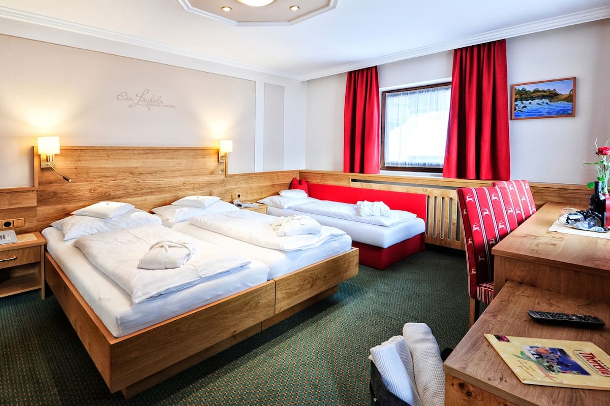 A hotel room with a large bed, two bedside tables, a desk with a chair, a window with red curtains, and a painting on the wall.