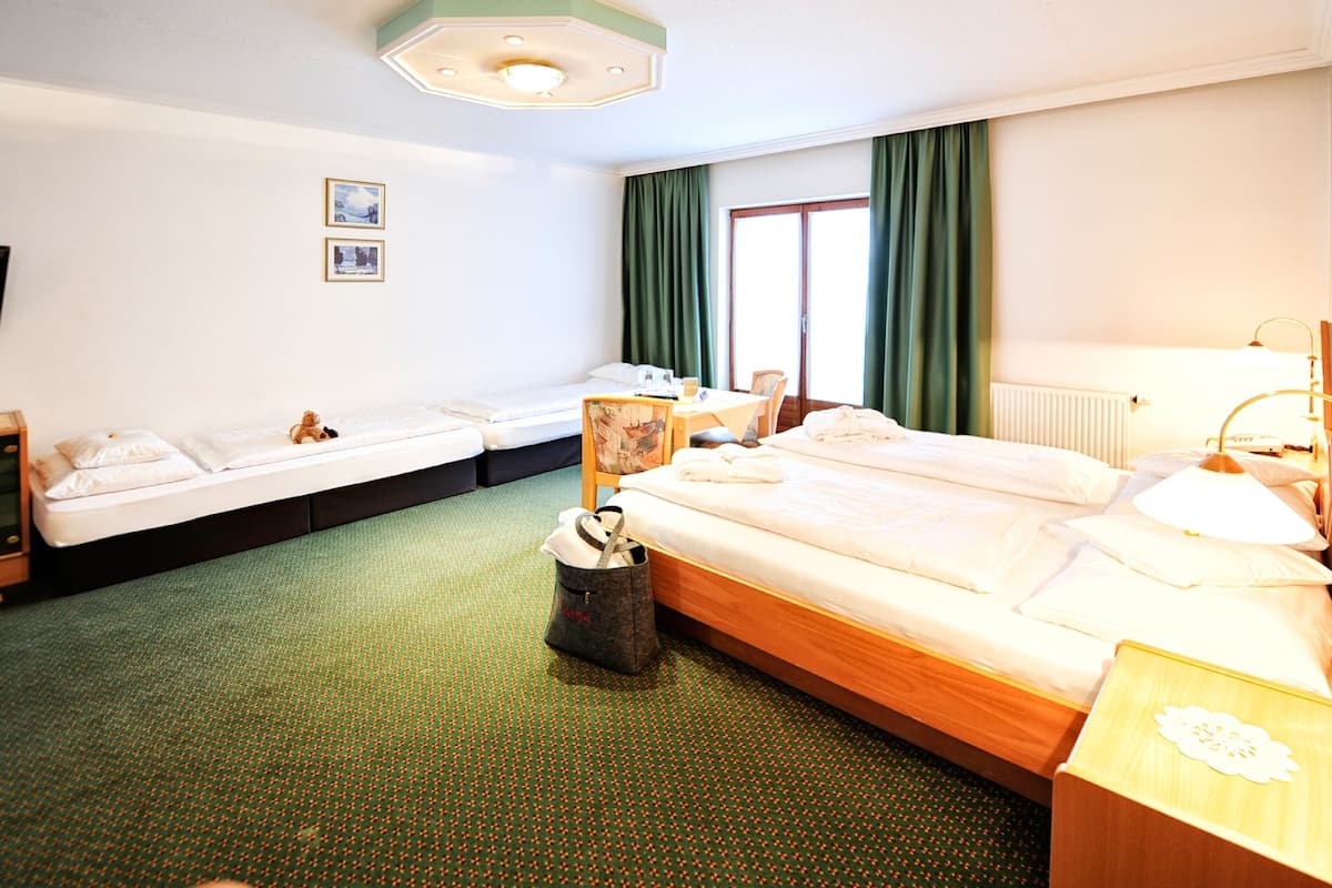 A hotel room with two single beds, a desk, a chair, a lamp, and a radiator.