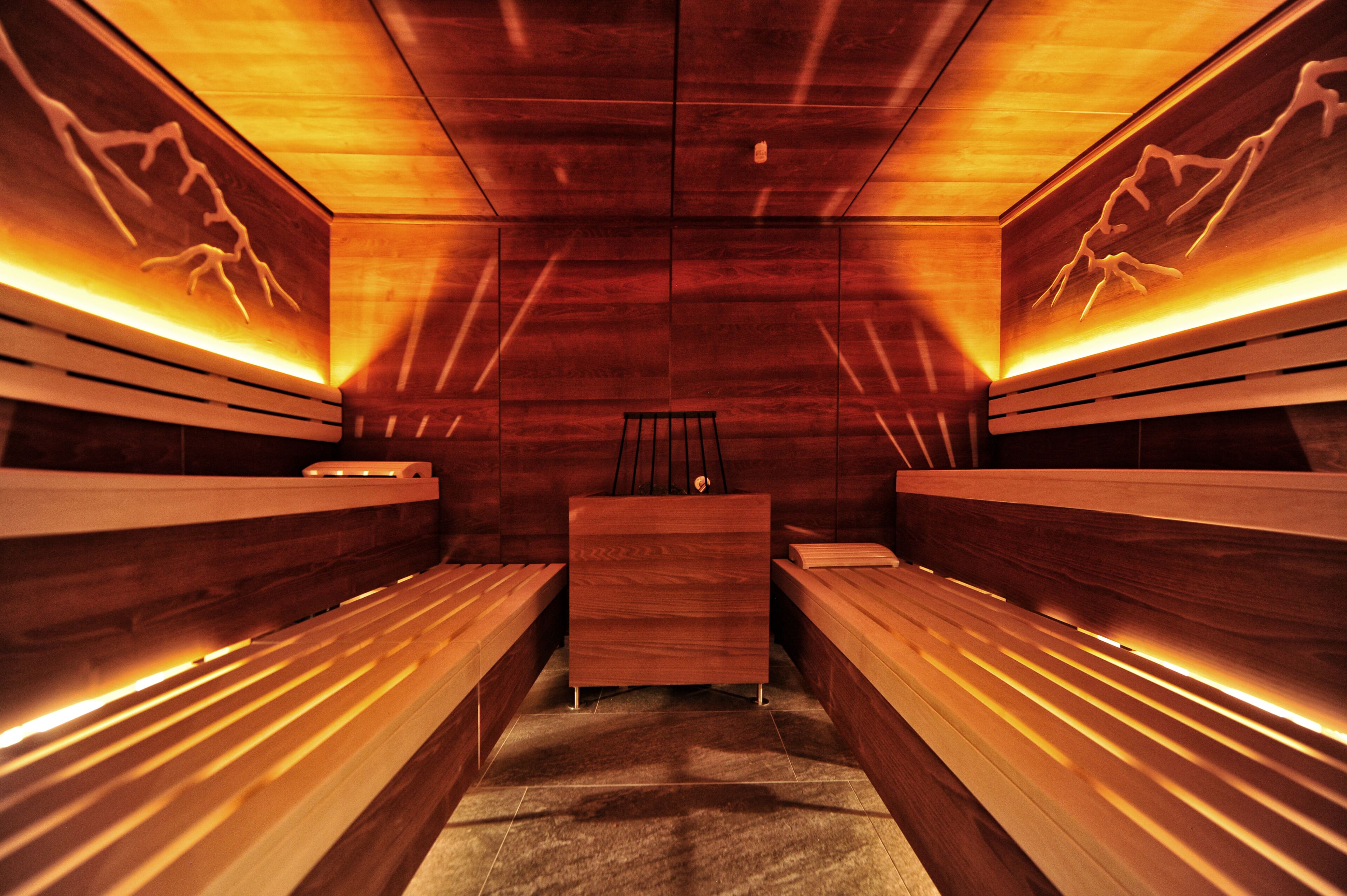 Eine Sauna mit Holzbänken und einem Tisch in der Mitte, beleuchtet durch warmes Licht.