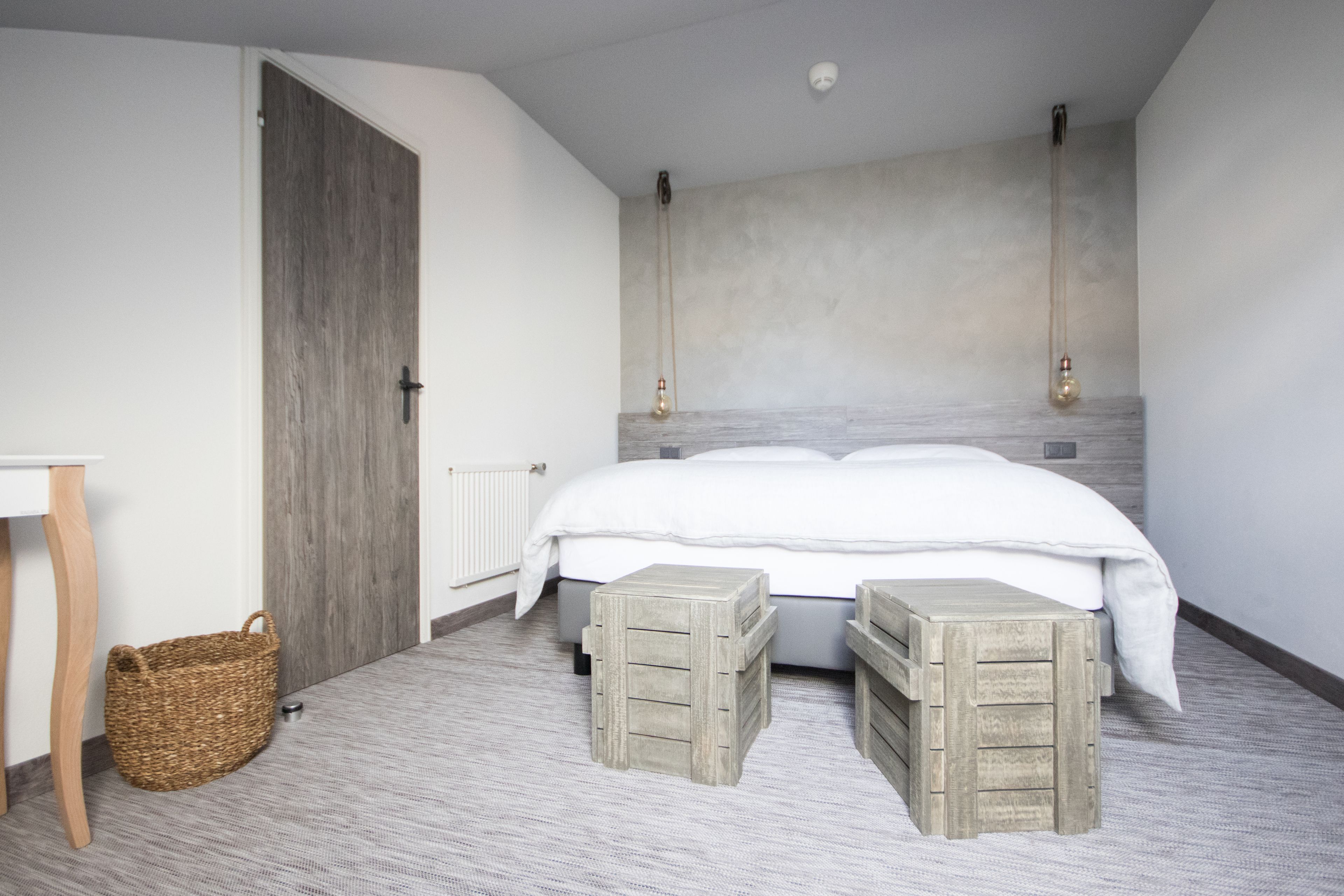 A bedroom with a bed, two wooden nightstands, a wicker basket, and a door.