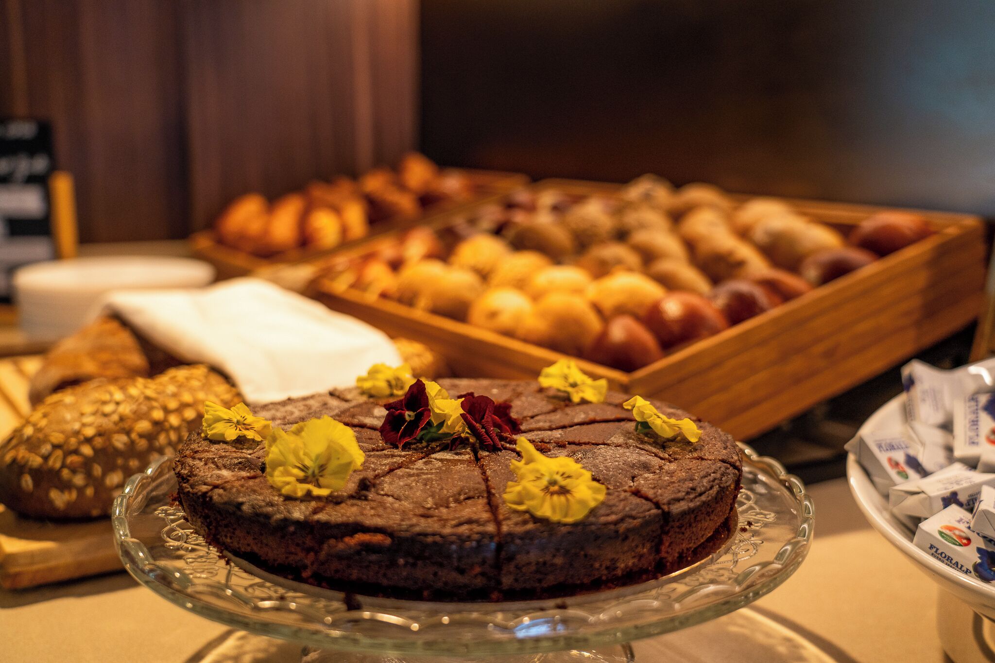 Un buffet con diverse preparazioni da forno e una torta al cioccolato decorata con fiori su un piedistallo di vetro.