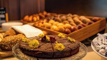 Un buffet con diverse preparazioni da forno e una torta al cioccolato decorata con fiori su un piedistallo di vetro.