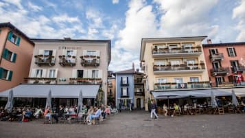 Une place publique dotée d’espaces de détente en plein air, un hôtel appelé « SEVEN BOUTIQUE HOTEL » avec des balcons, et un restaurant appelé « RISTORANTE at Fara ».