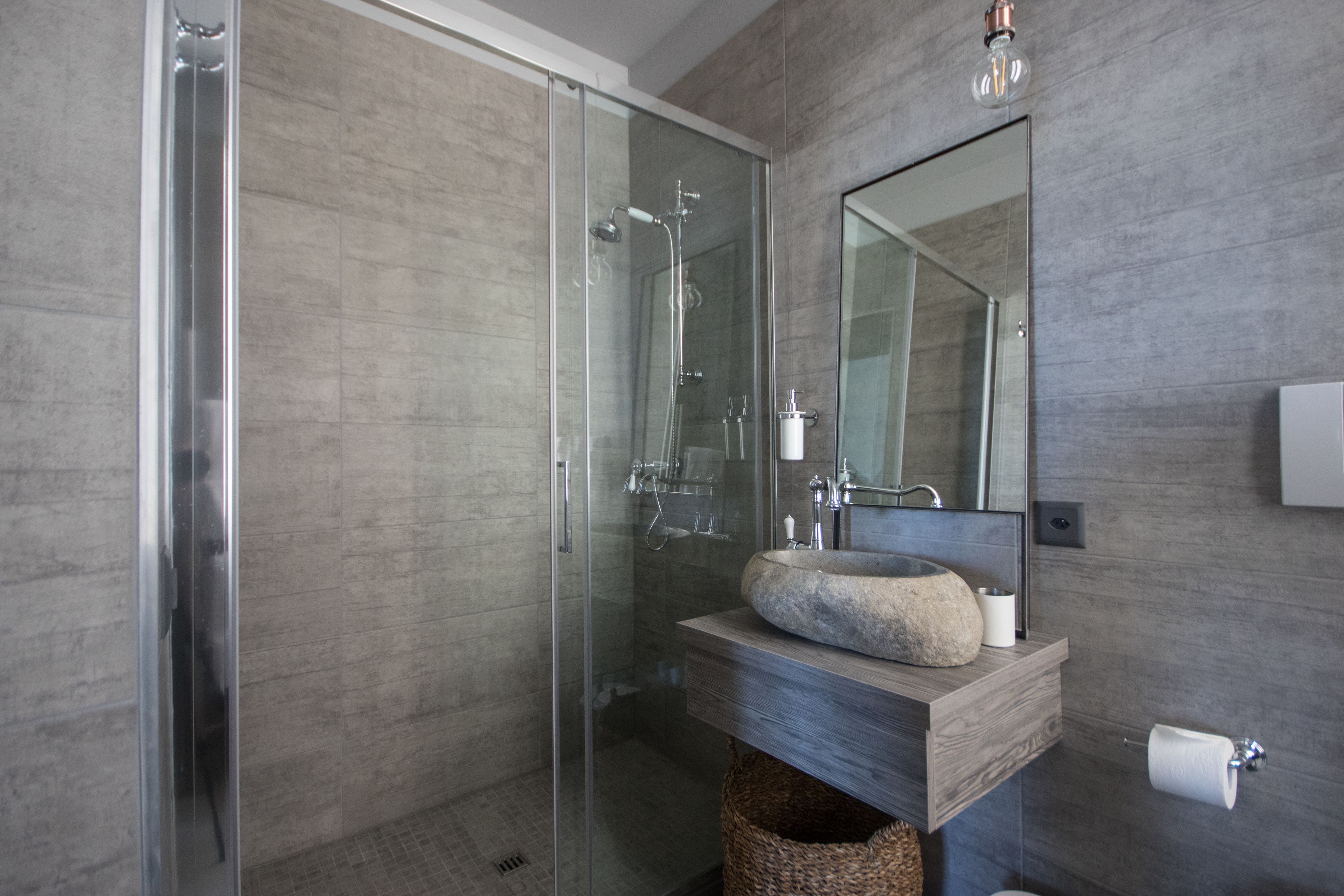 Un baño moderno con ducha de vidrio, tocador de madera con lavamanos de piedra y un espejo grande.