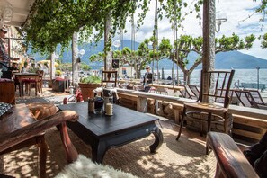An outdoor seating area with wooden furniture, a table with a candle, and a view of the lake and mountains. - Seven Boutique Hotel (Ascona)