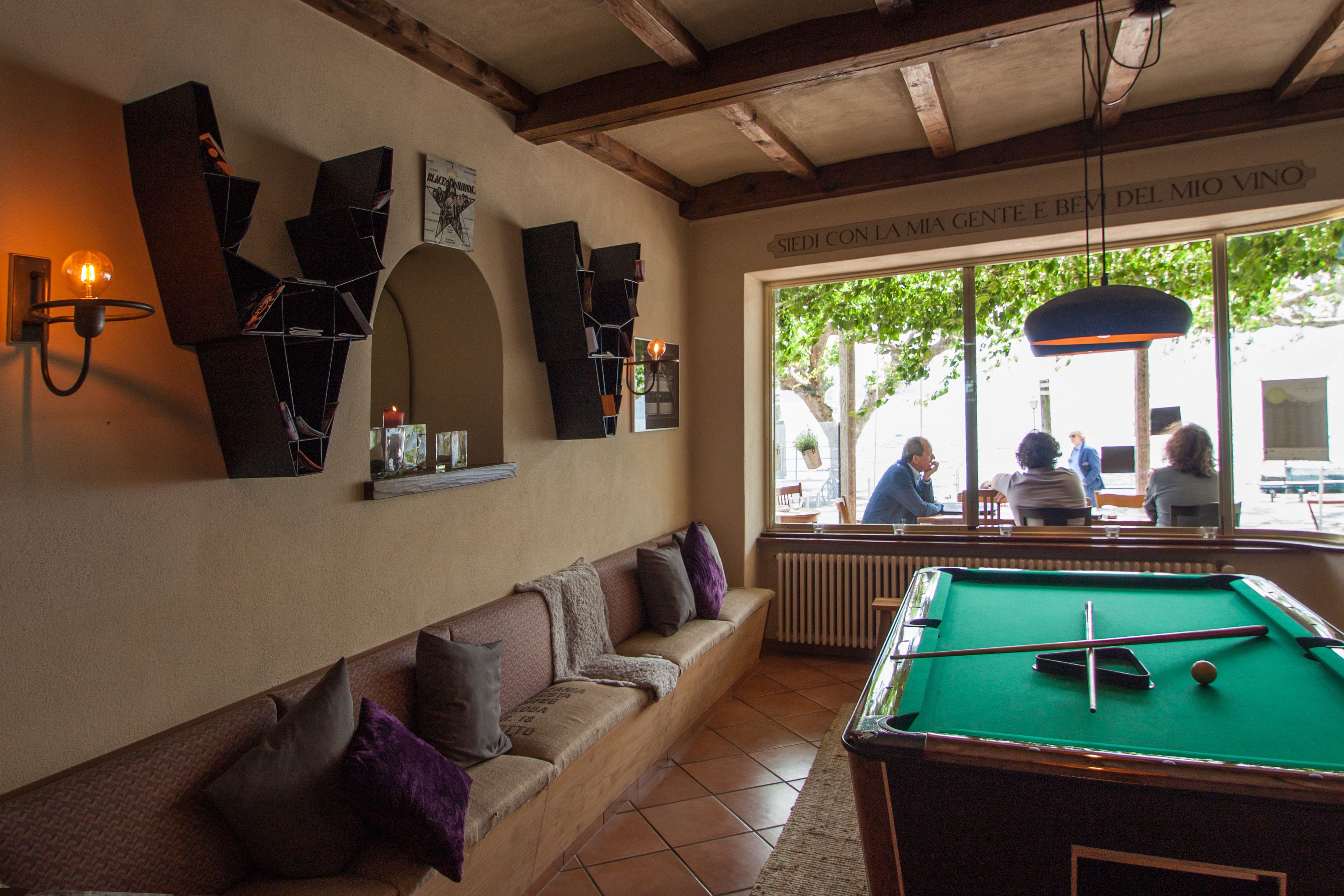 A billiards table with a pool cue and balls, a sofa with cushions, and a wall-mounted shelf with books and a lamp.