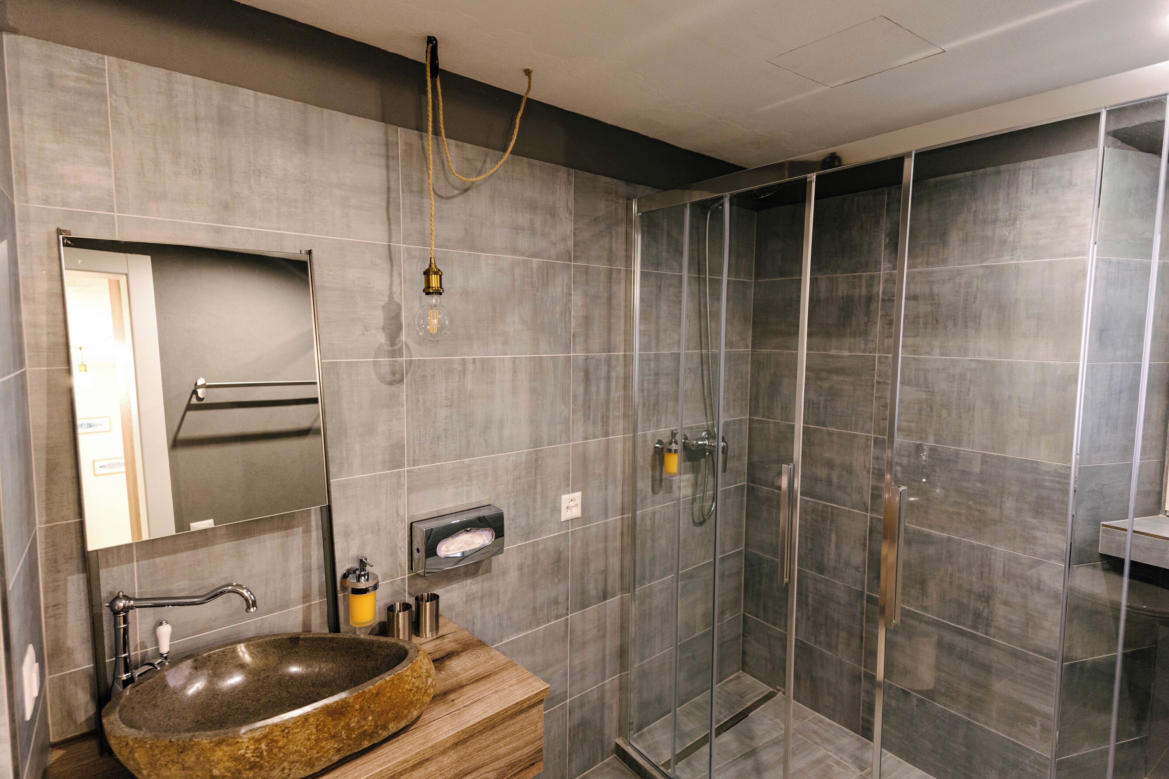 Un baño moderno con un lavamanos grande de granito, un espejo, un perchero para toallas y una zona de ducha con paredes de vidrio.