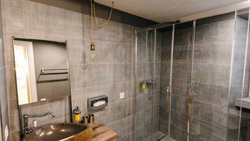Un baño moderno con un lavamanos grande de granito, un espejo, un perchero para toallas y una zona de ducha con paredes de vidrio.