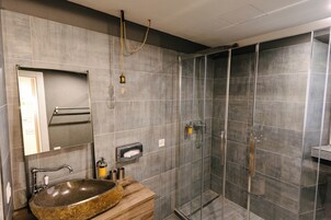 Un baño moderno con un lavamanos grande de granito, un espejo, un perchero para toallas y una zona de ducha con paredes de vidrio.