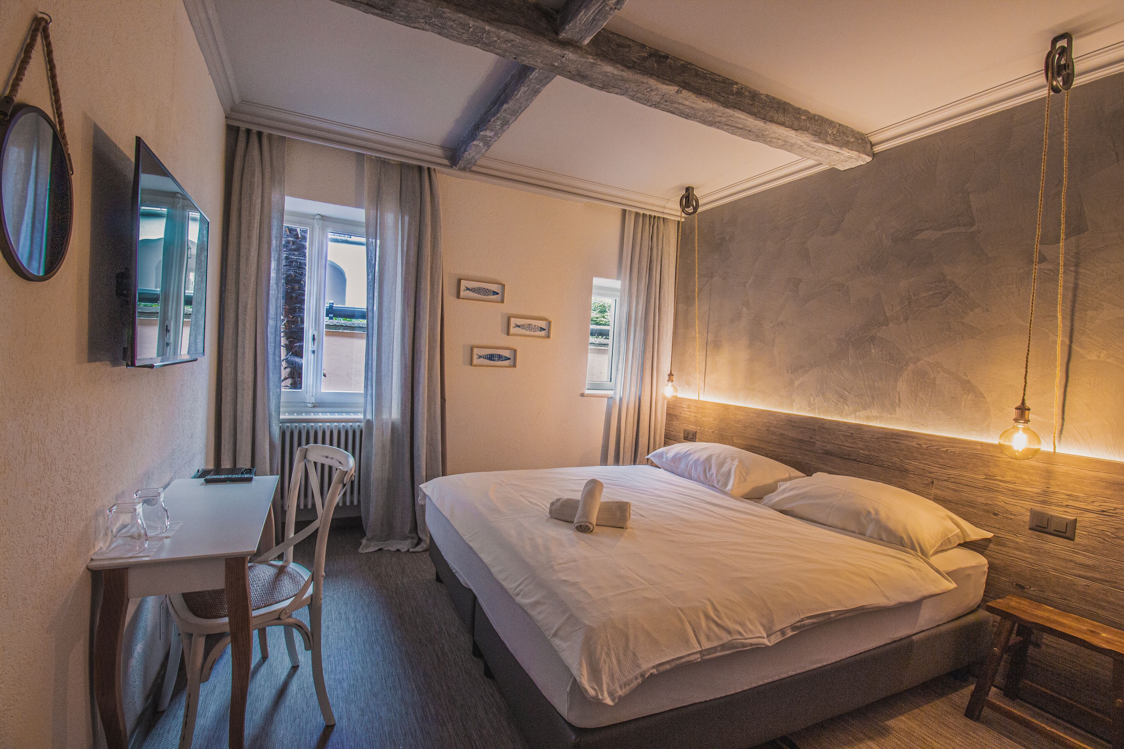 A hotel room with a bed, a desk, a chair, and a window with curtains.