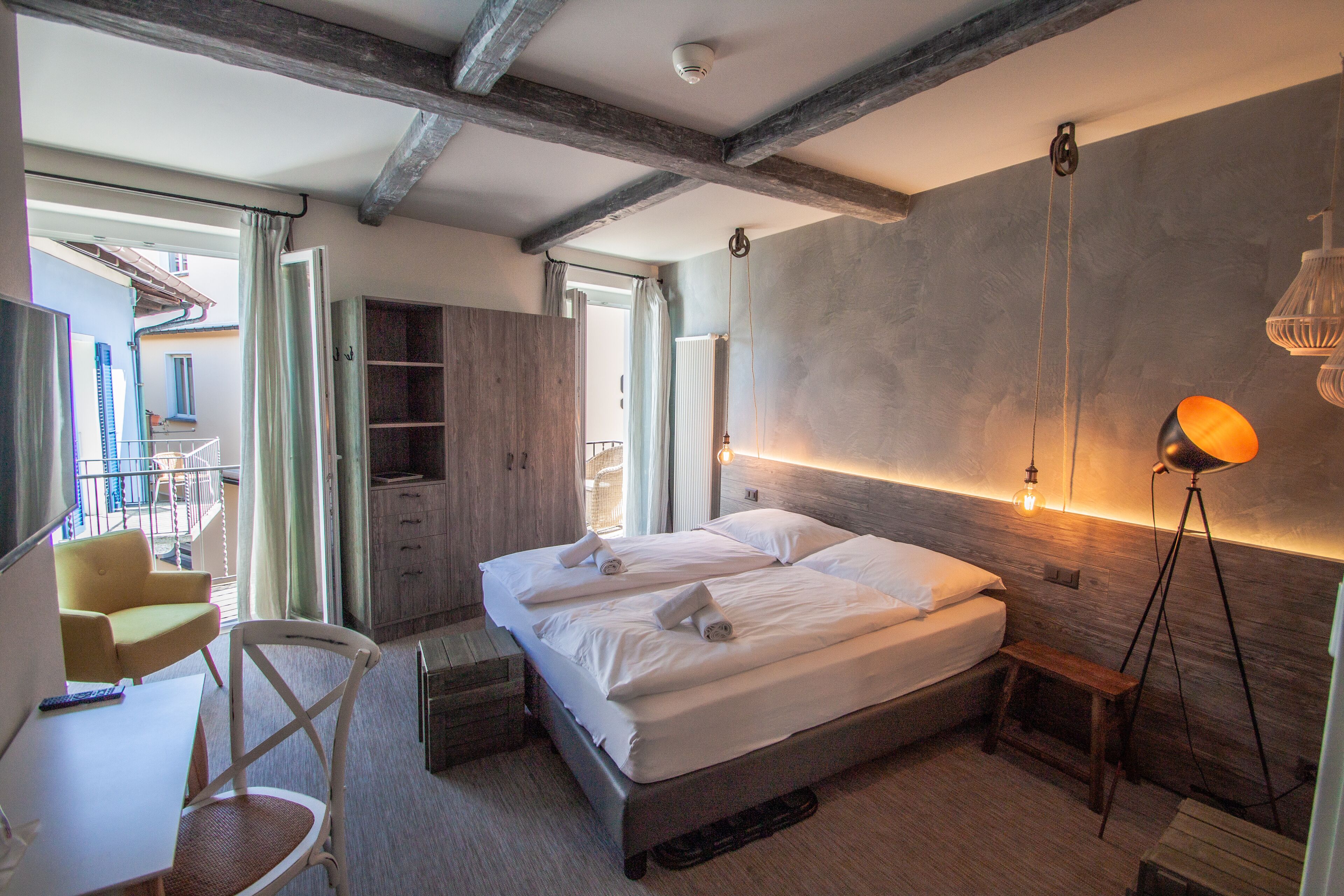 Un dormitorio con cama, mesita de noche, silla y vistas al balcón.