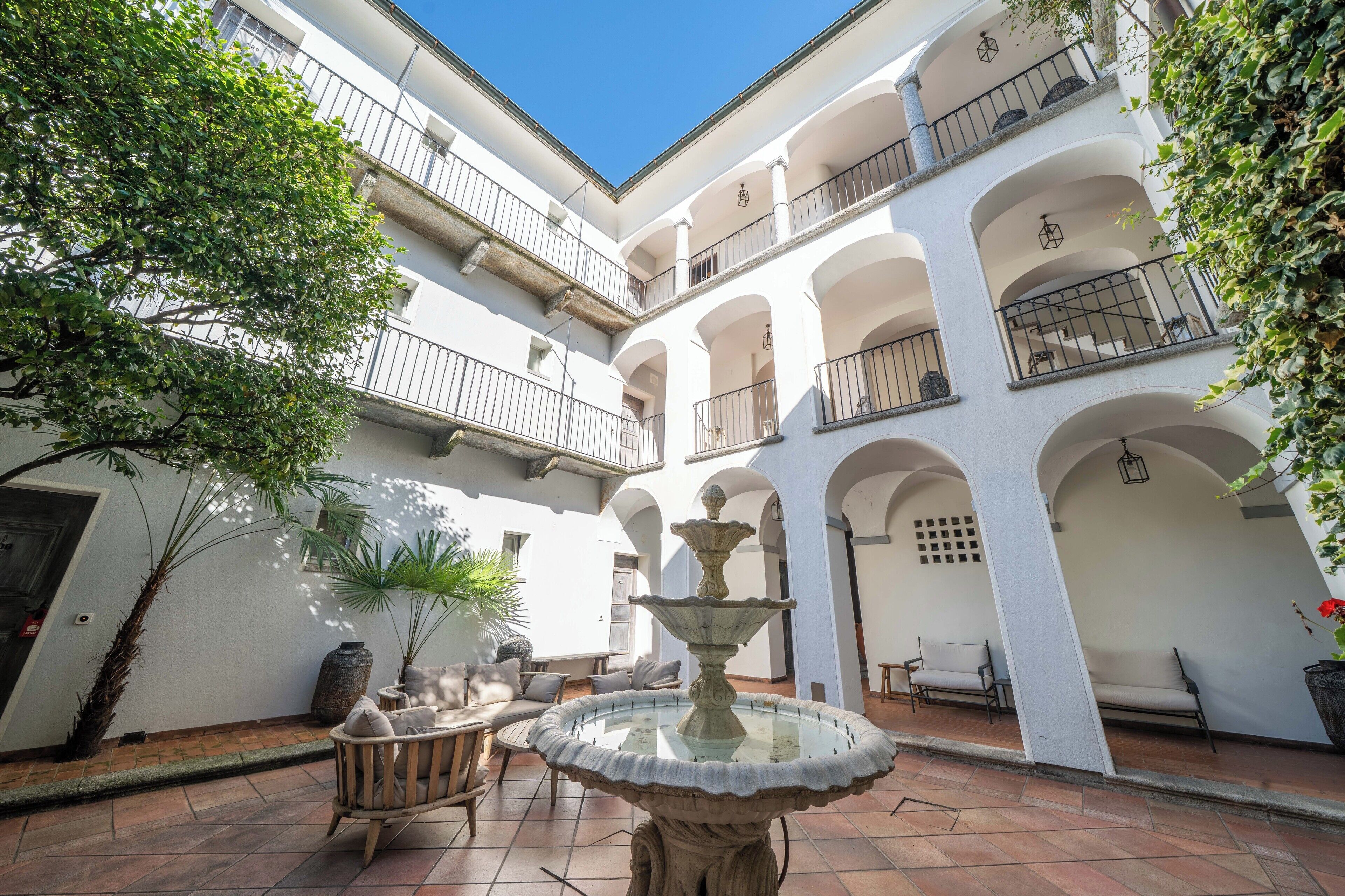 A courtyard with a fountain, seating, and a white building with balconies.