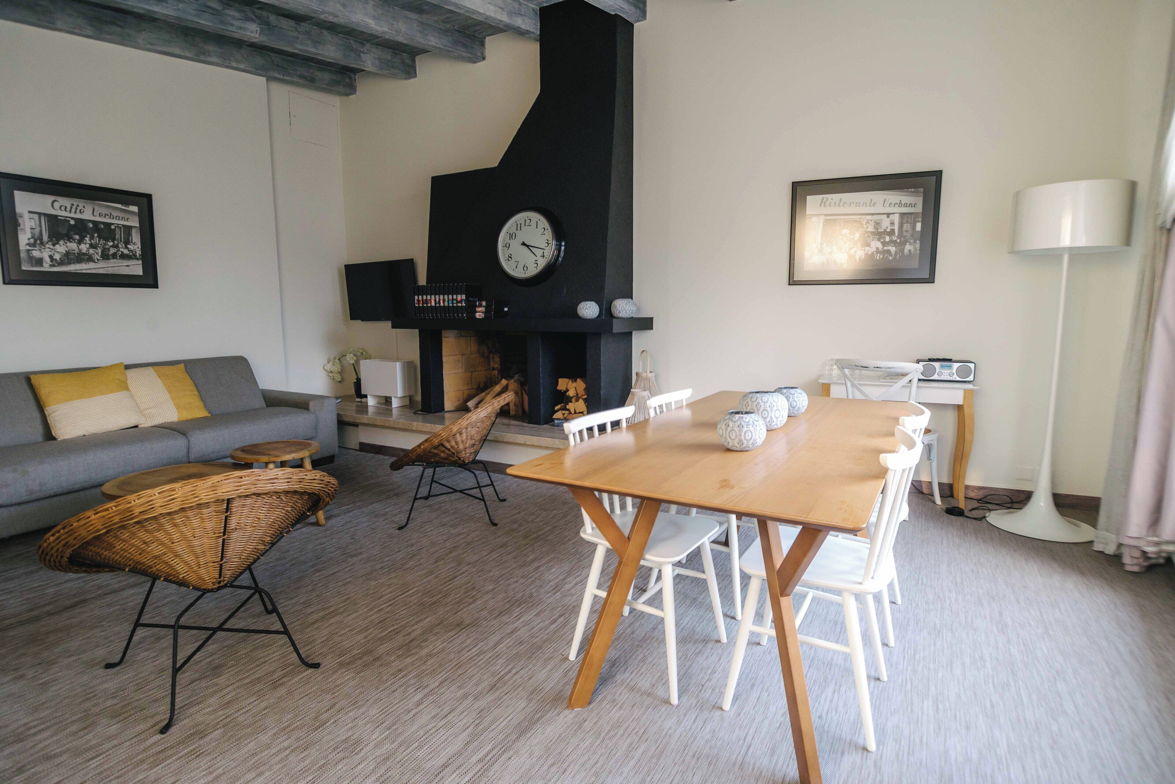 A living room with a wooden table, white chairs, a sofa, and a black fireplace.