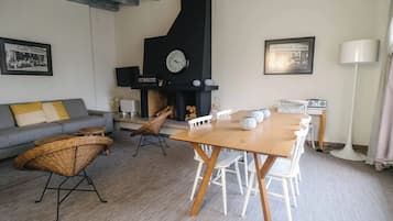 A living room with a wooden table, white chairs, a sofa, and a black fireplace.