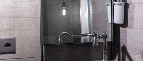 A modern bathroom with a stone sink, a large mirror, and a light fixture.
