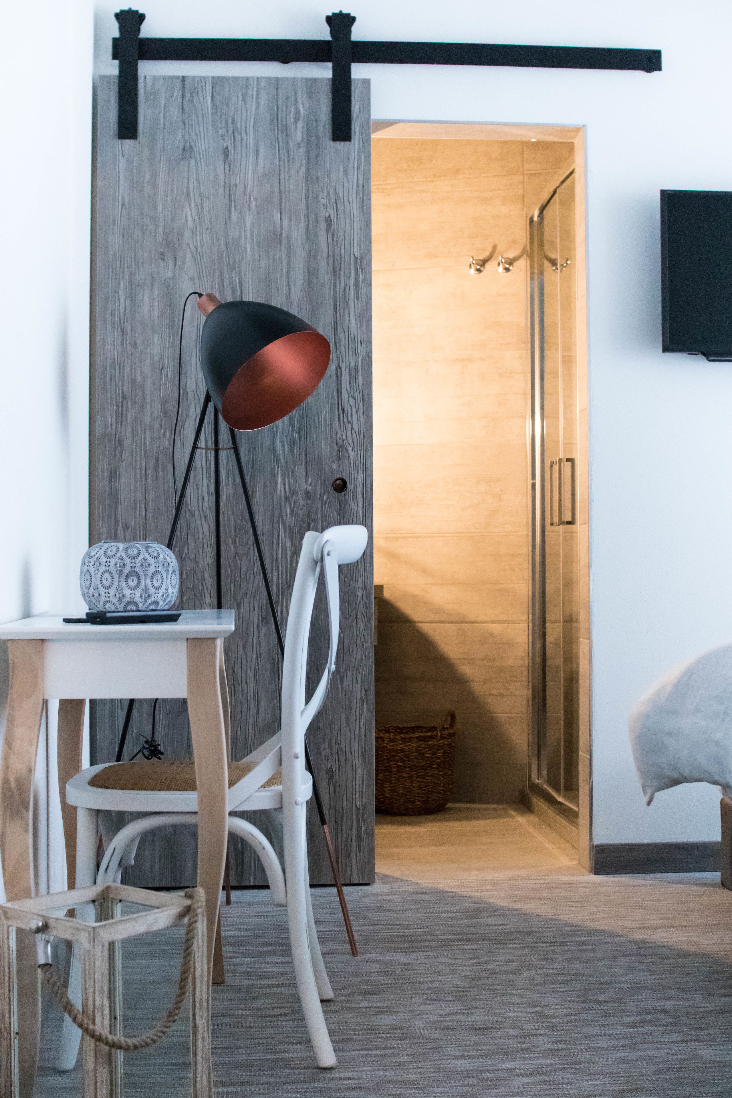 Une pièce dotée d’une porte coulissante en bois, d’une chaise blanche, d’une table avec une lampe et d’une cabine de douche en verre.