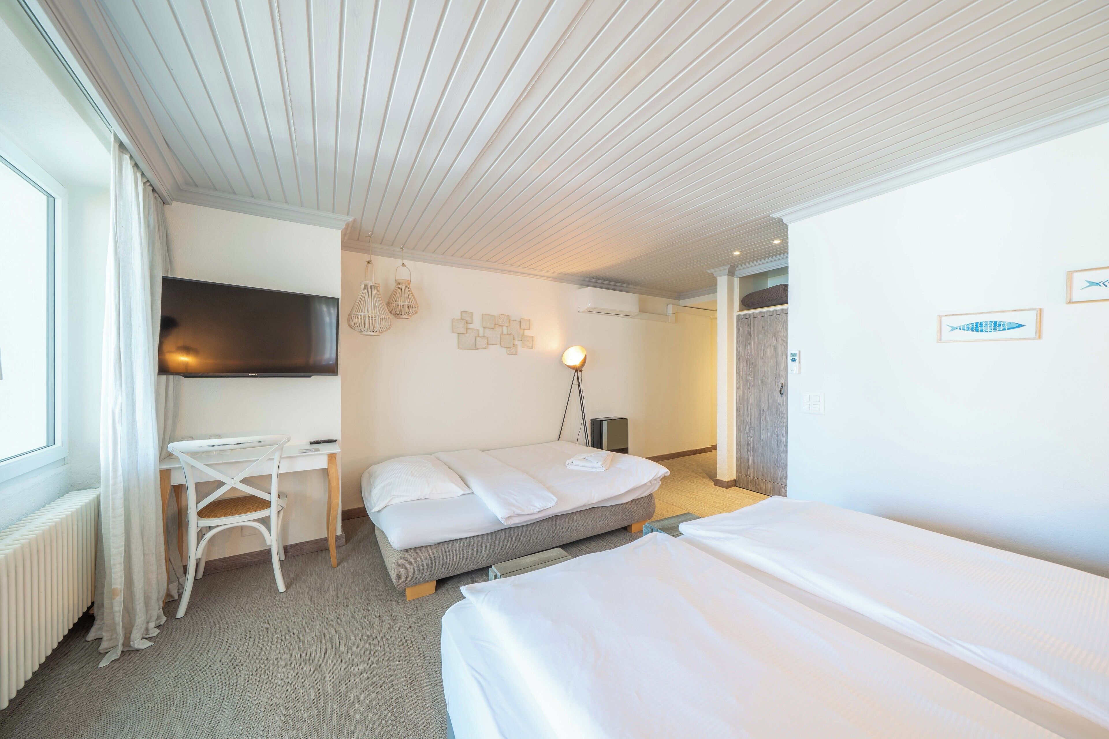 A hotel room with a bed, a desk, a chair, a TV, and a lamp.