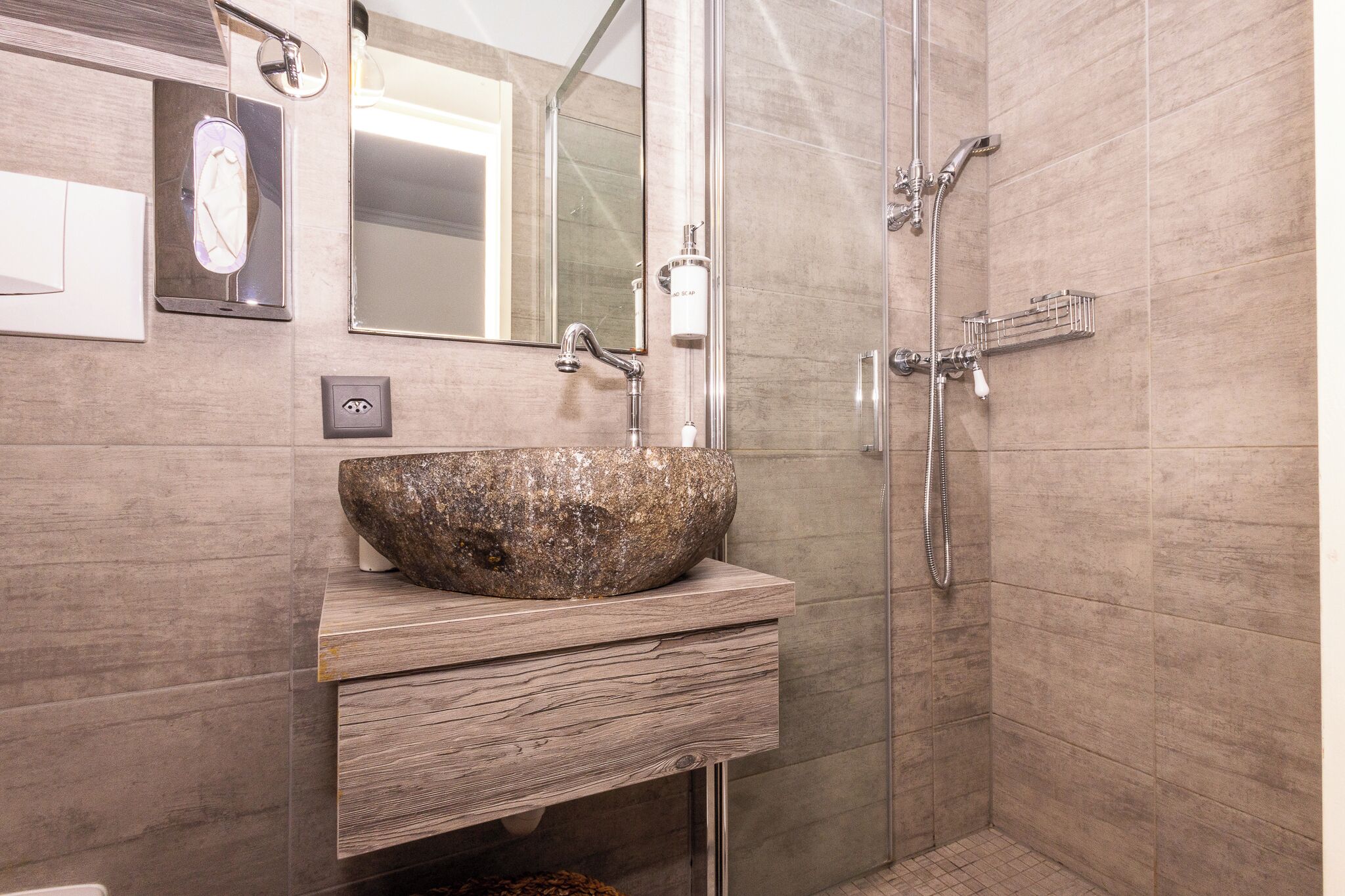 A modern bathroom with a stone sink, a large mirror, and a walk-in shower with a handheld showerhead.