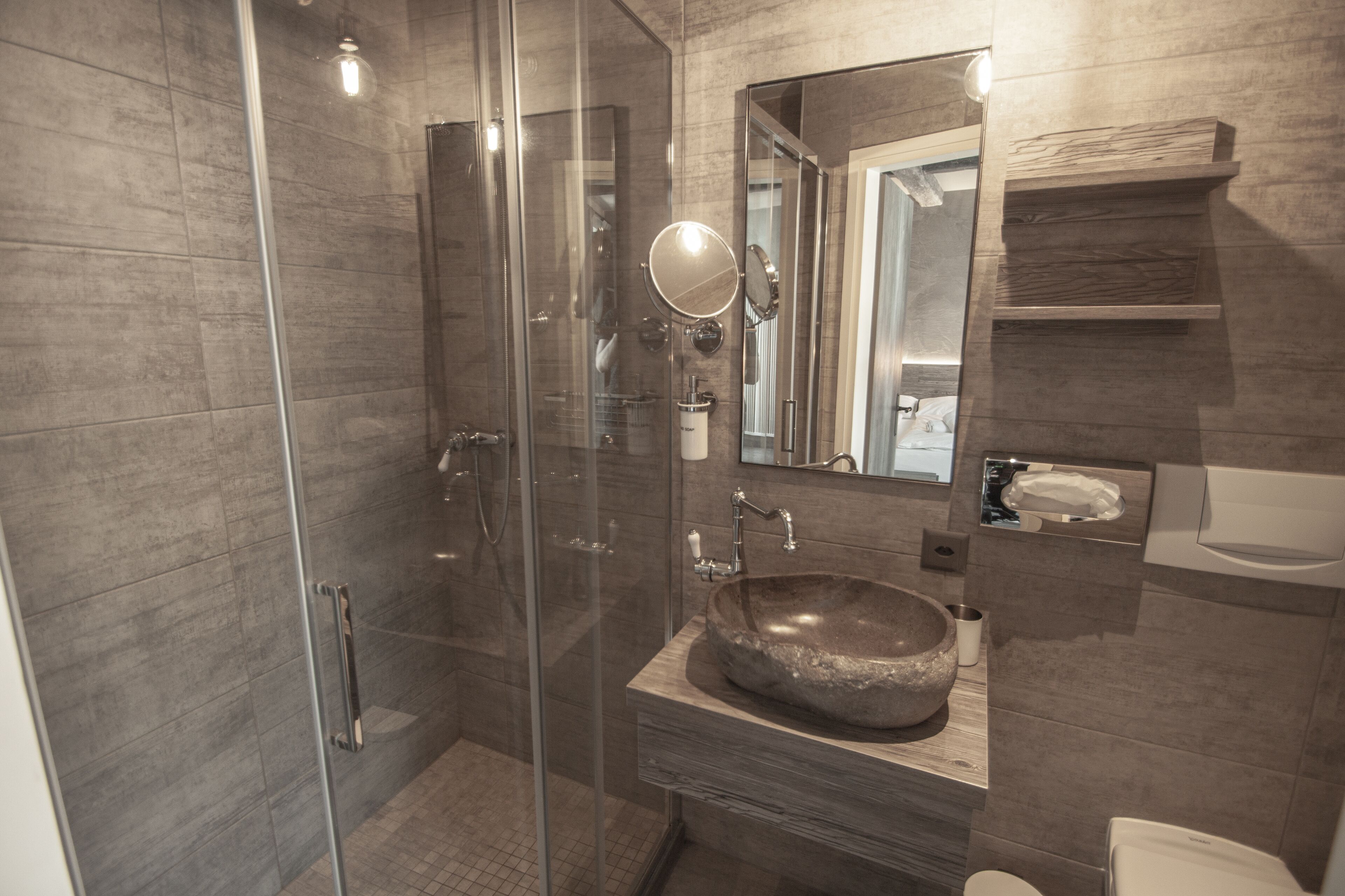 Une salle de bain moderne avec une douche à parois de verre, un meuble-lavabo en bois doté d’un grand évier et un miroir au-dessus de l’évier.