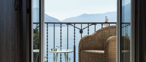 Ein Balkon mit einem Korbstuhl und einem kleinen Tisch mit Blick auf ein Gewässer und Berge.