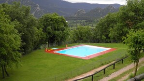 A rectangular pool with a red border, surrounded by a grassy area and trees, with mountains in the background. - Camping Morunys (Sant Llorenc de Morunys)