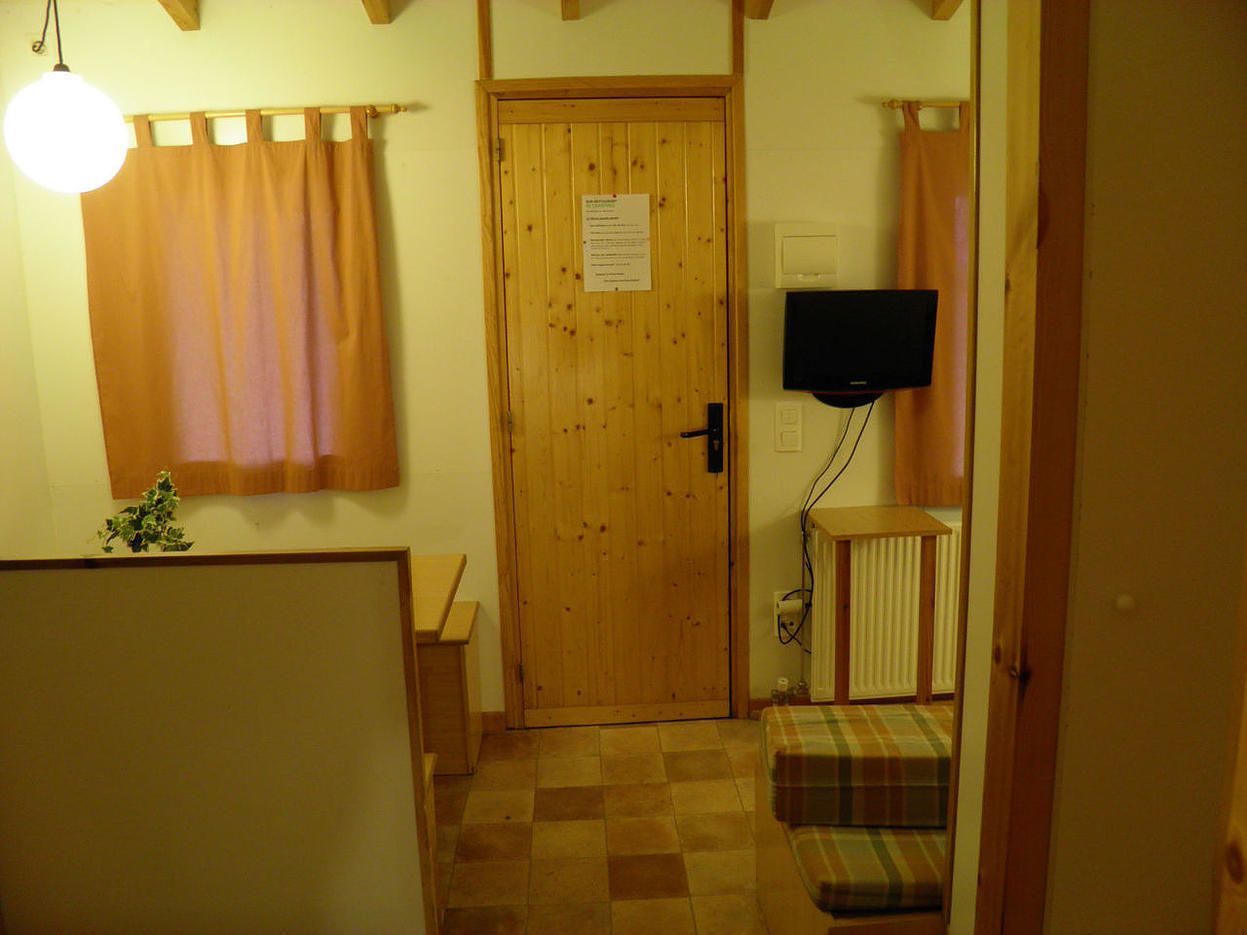 A room with a wooden door, a television mounted on the wall, a small bench, and a radiator.