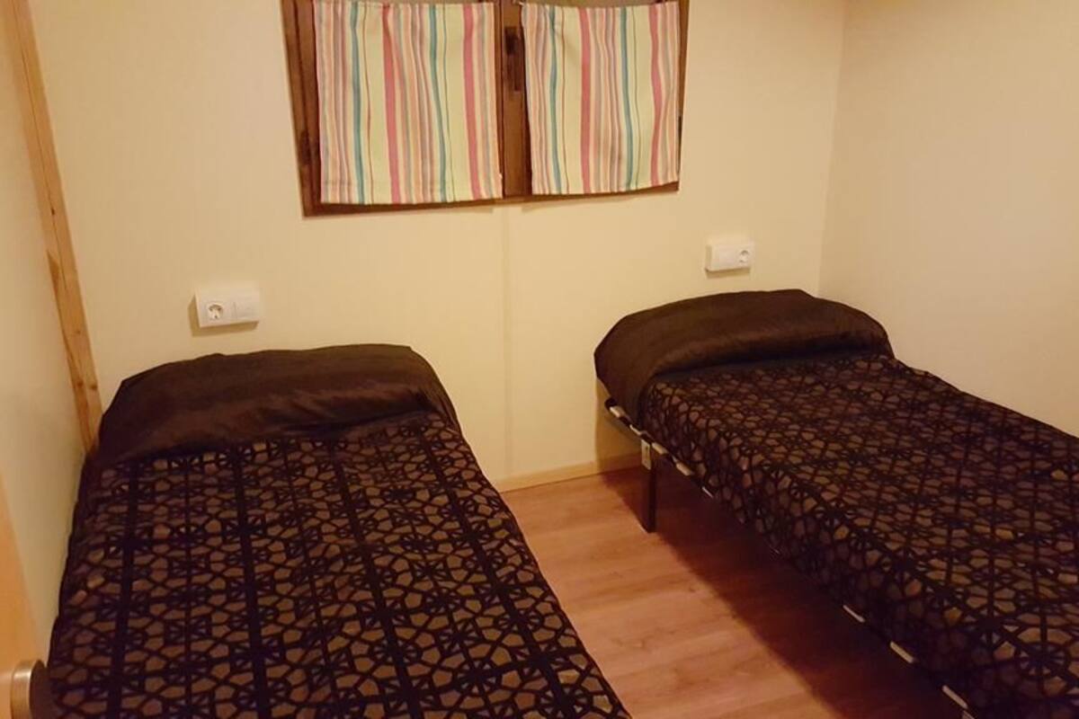 Una habitación pequeña con dos camas individuales, piso de madera y una ventana con cortinas a rayas.