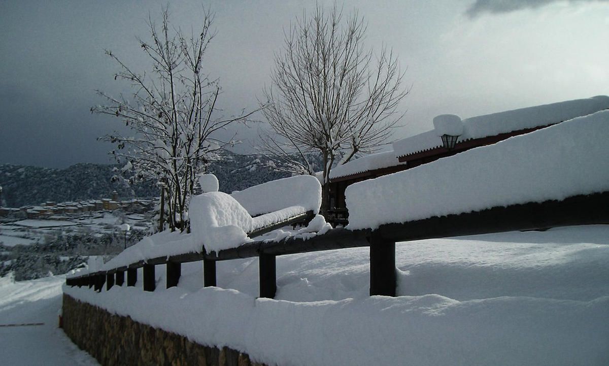 A snow-covered landscape with a wooden fence and bare trees.