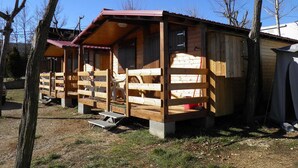 A row of wooden cabins with attached porches, each with a bench and a small table. - Camping Morunys (Sant Llorenc de Morunys)