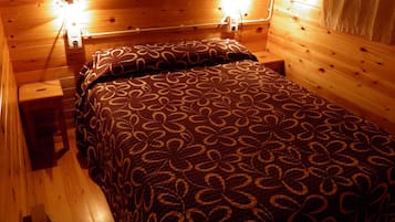 A wooden cabin-style room with a bed, two bedside lamps, and a nightstand.
