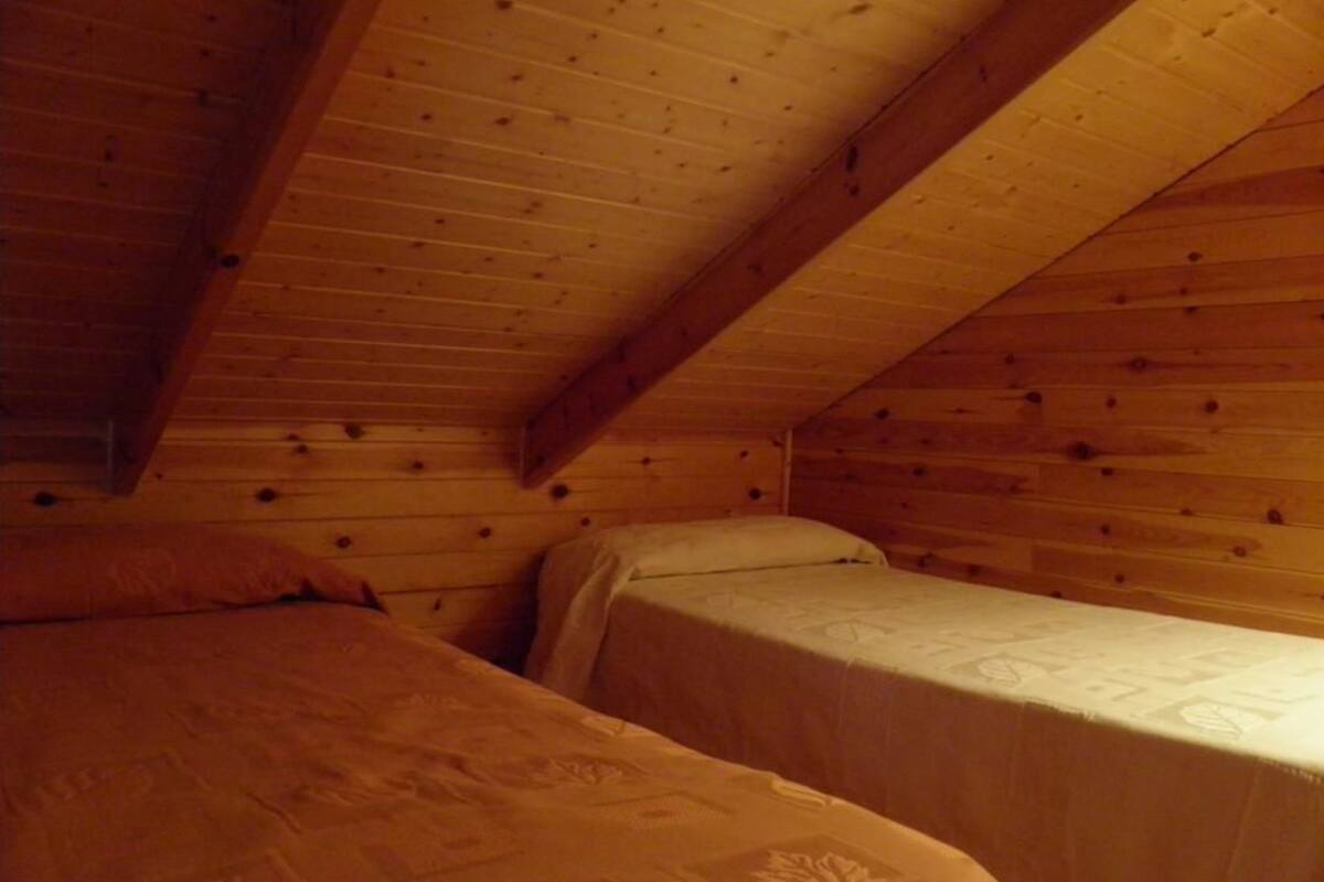 Una habitación pequeña y acogedora con dos camas, paredes de madera y techo inclinado.