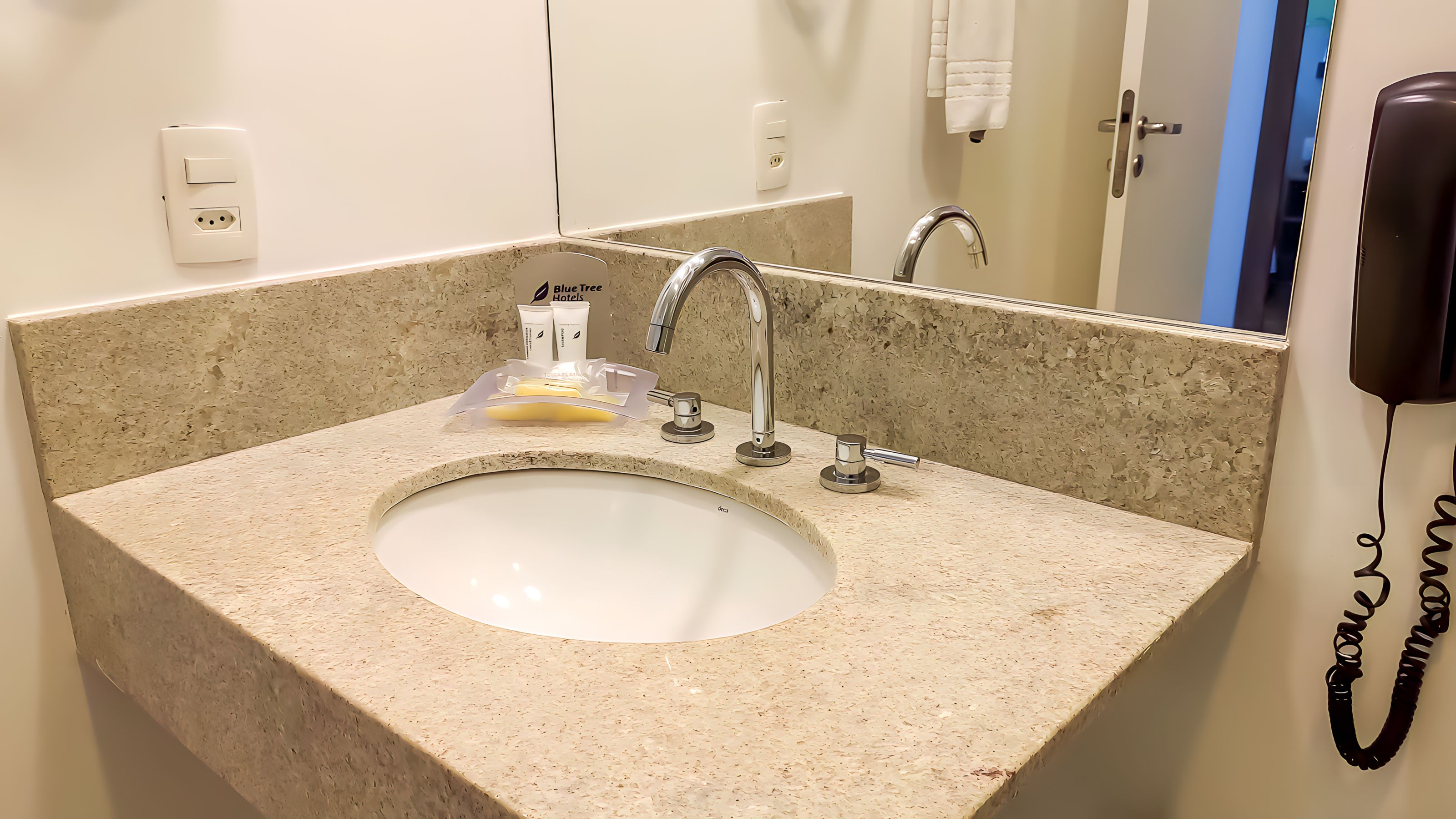 A bathroom sink with a granite countertop, a mirror, a towel dispenser, and a phone.