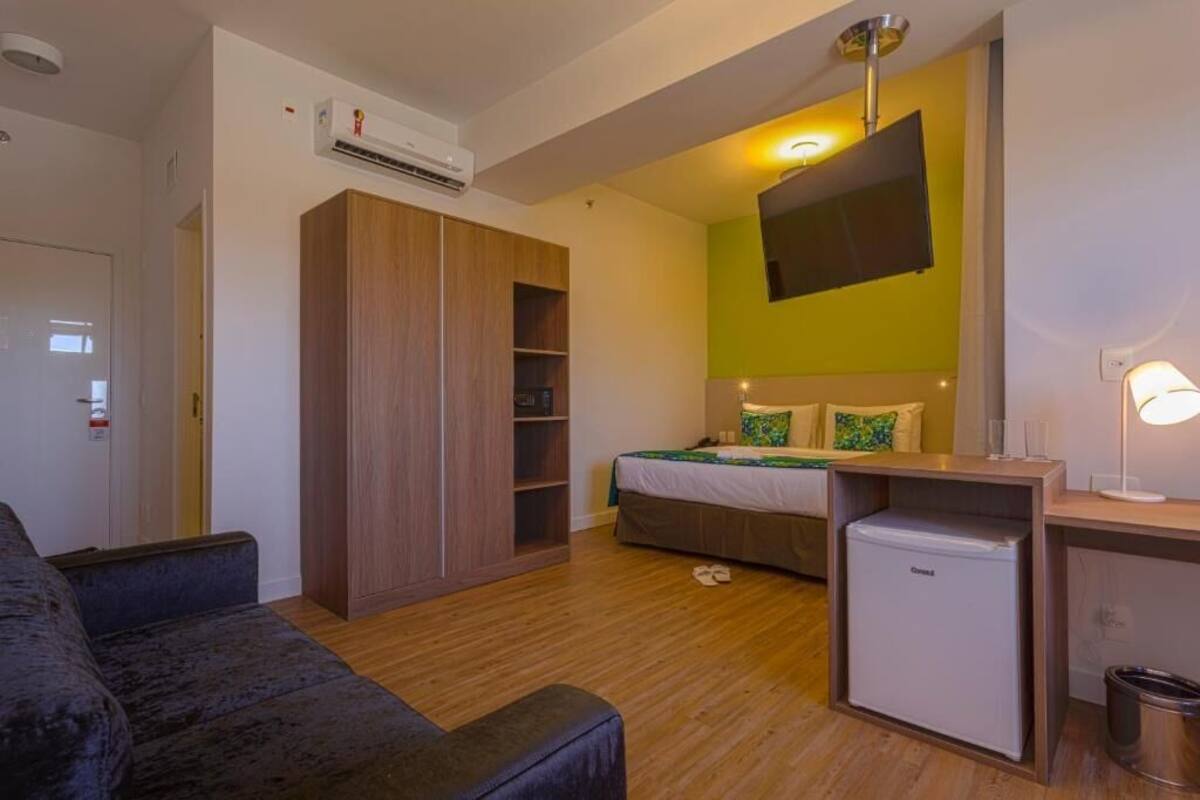 Een kleine hotelkamer met een bed, een bureau, een kledingkast en een aan de muur bevestigde televisie.