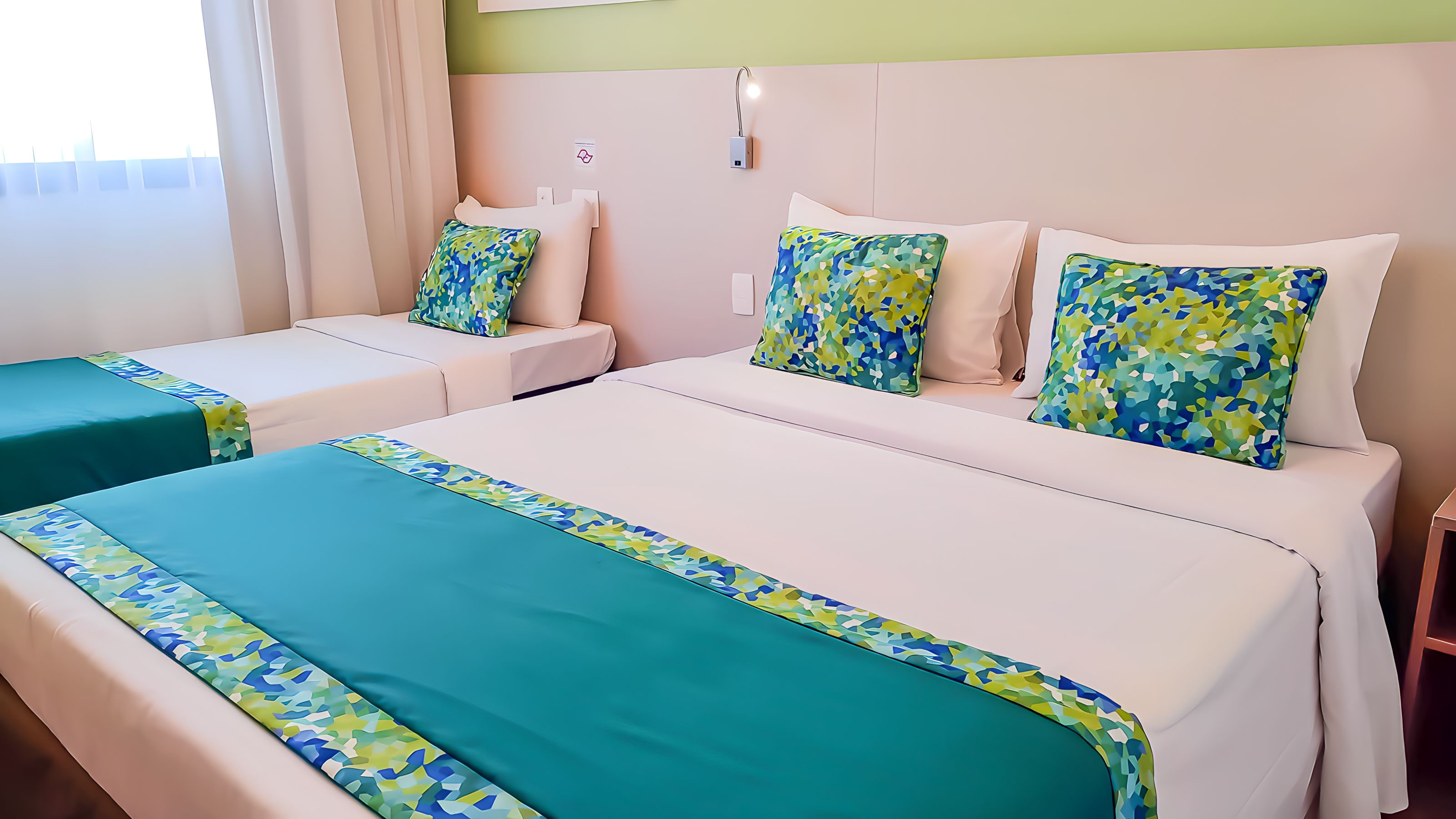 A hotel room with two beds, each with a teal bedspread and matching pillows.