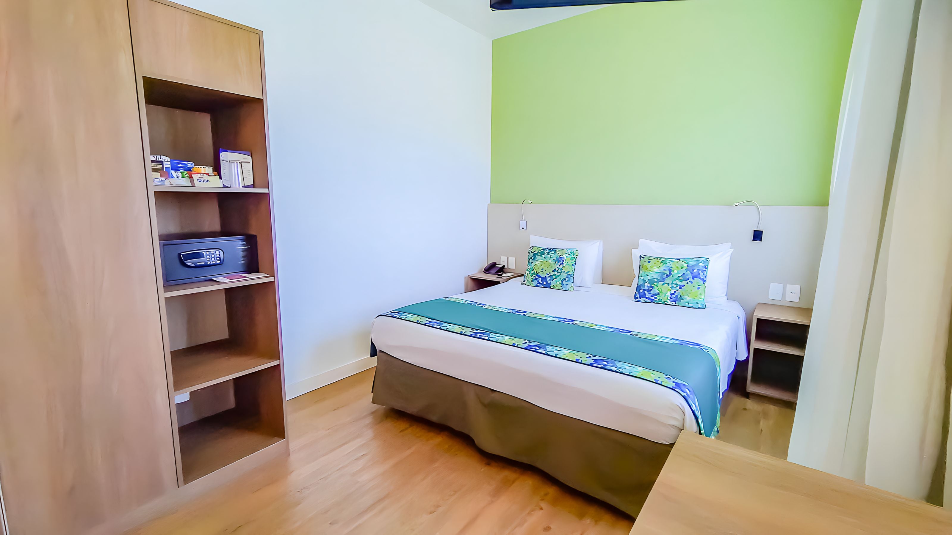A hotel room with a bed, a wooden wardrobe, and a green accent wall.