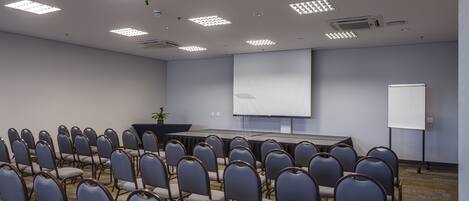 A conference room with rows of chairs, a projector screen, and a whiteboard.