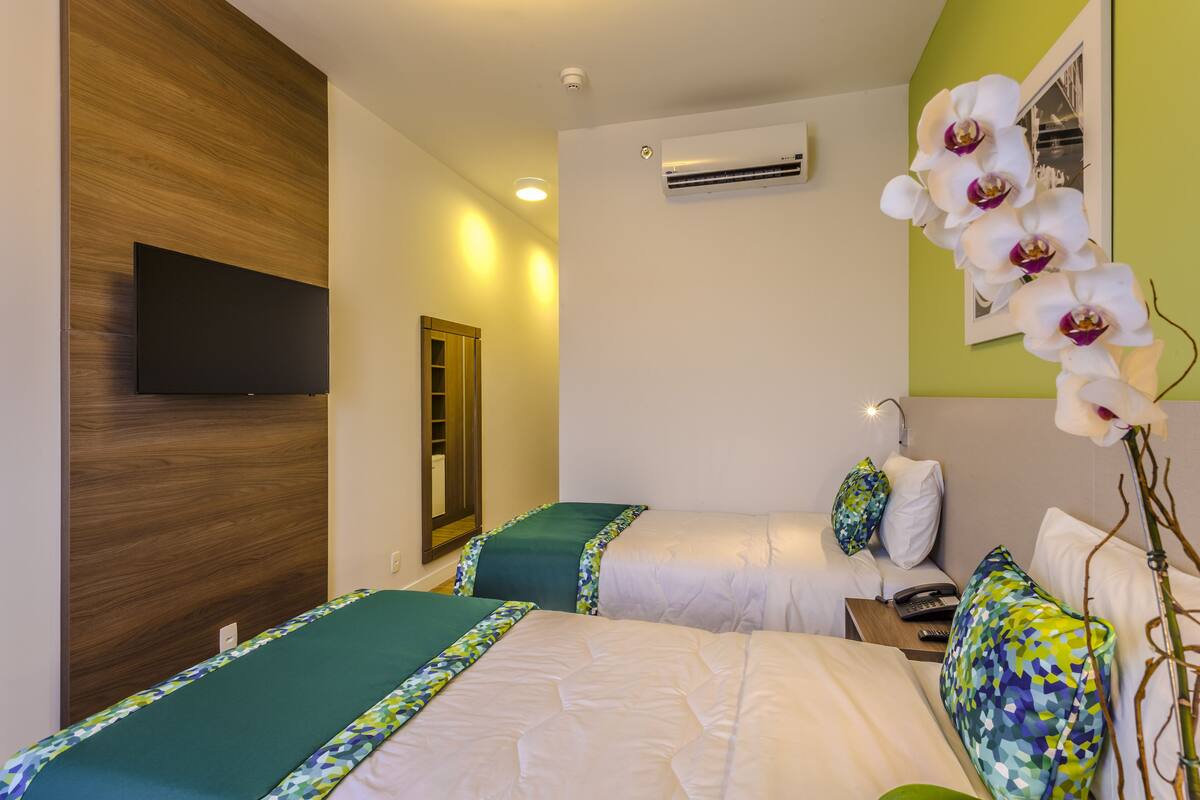 Een hotelkamer met twee bedden, een flatscreen televisie, airconditioning en een spiegel aan de muur.
