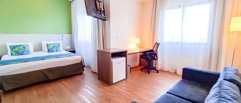 Una habitación de hotel con cama, escritorio, silla y sofá.