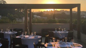 An outdoor dining area with tables set for a meal, overlooking a cityscape during sunset. - Blue Tree Towers Valinhos (Valinhos)