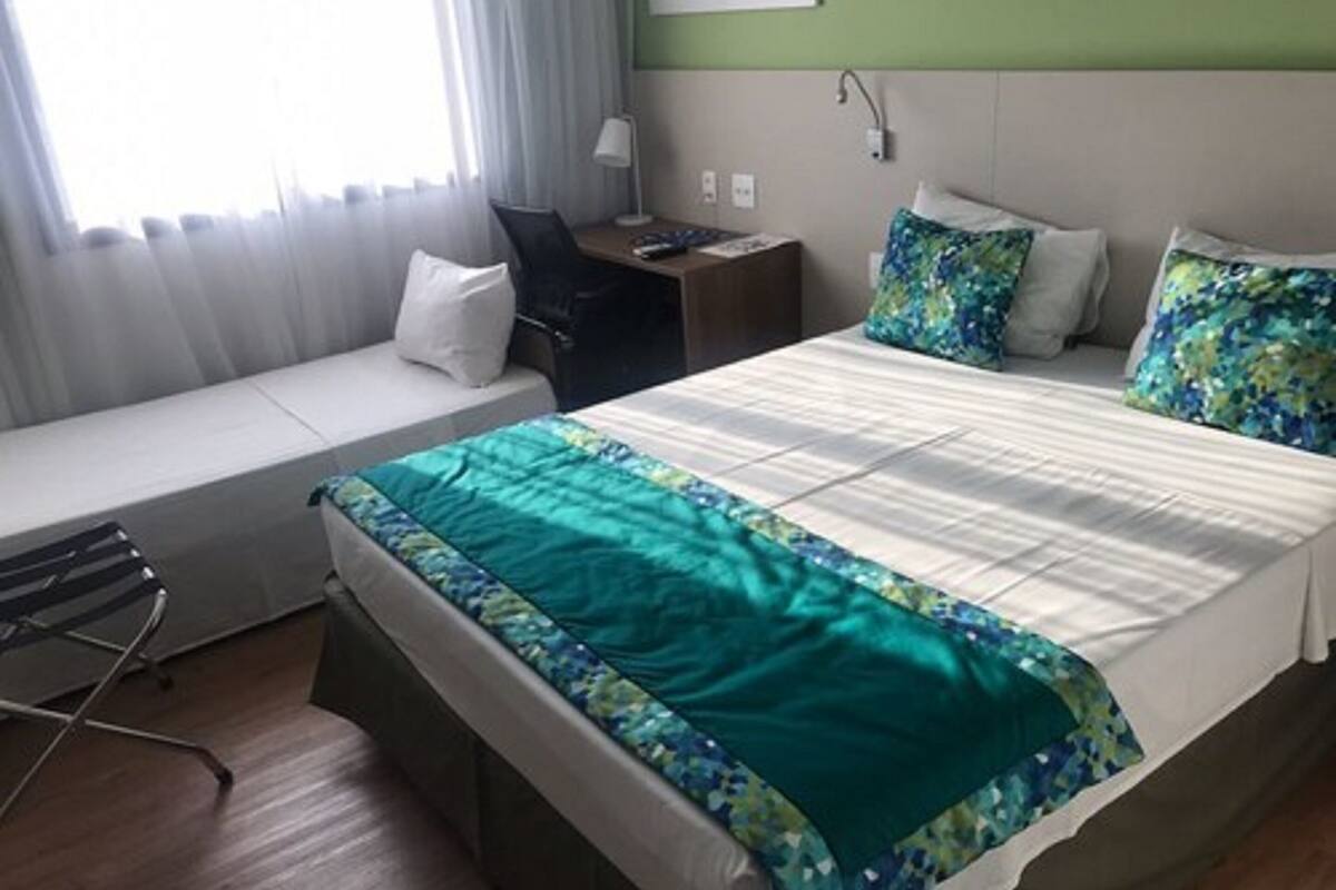 Een hotelkamer met een bed, een bureau, een stoel en een raam met gordijnen.