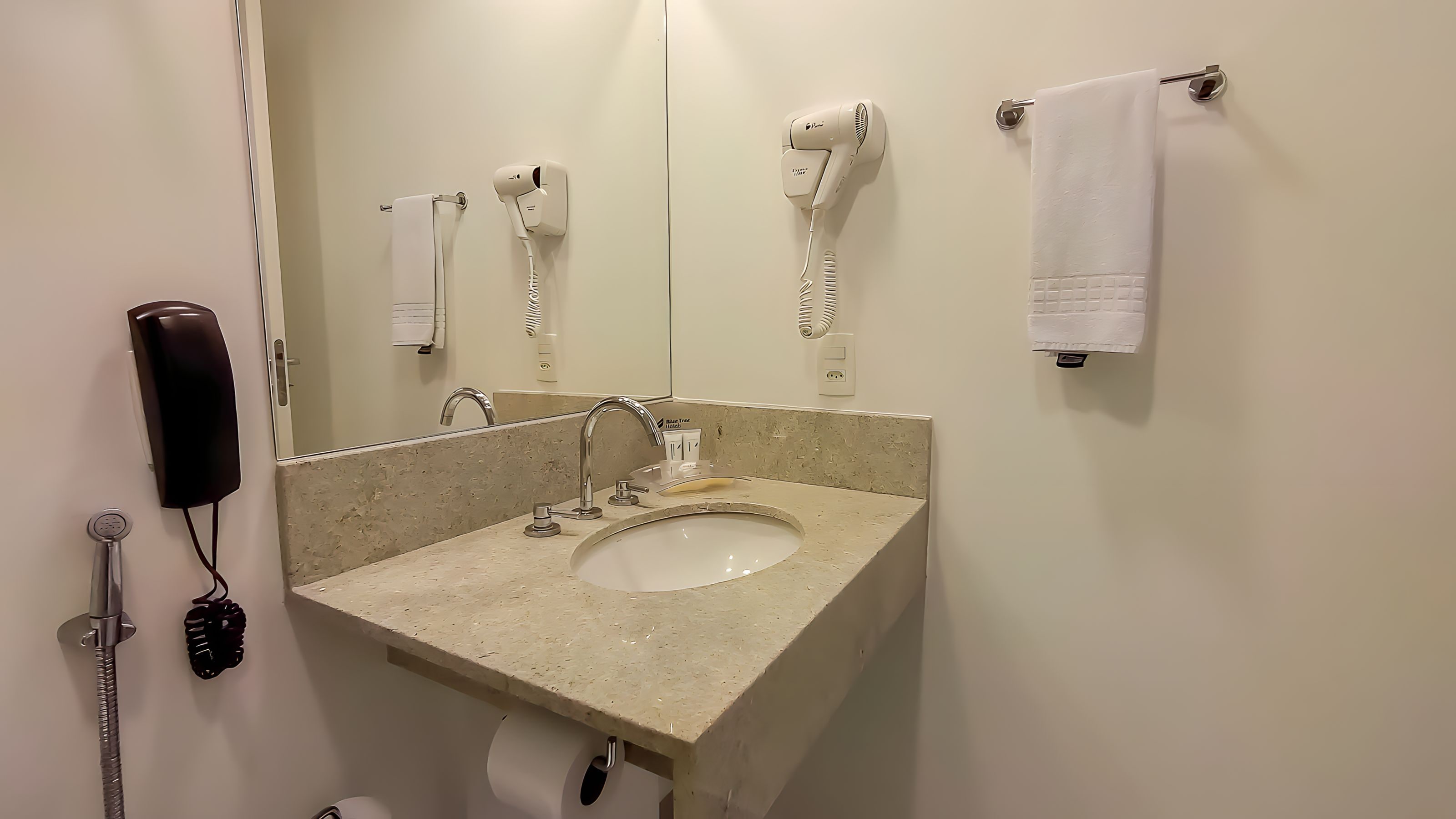 A bathroom with a sink, mirror, towel rack, hair dryer, and a phone.