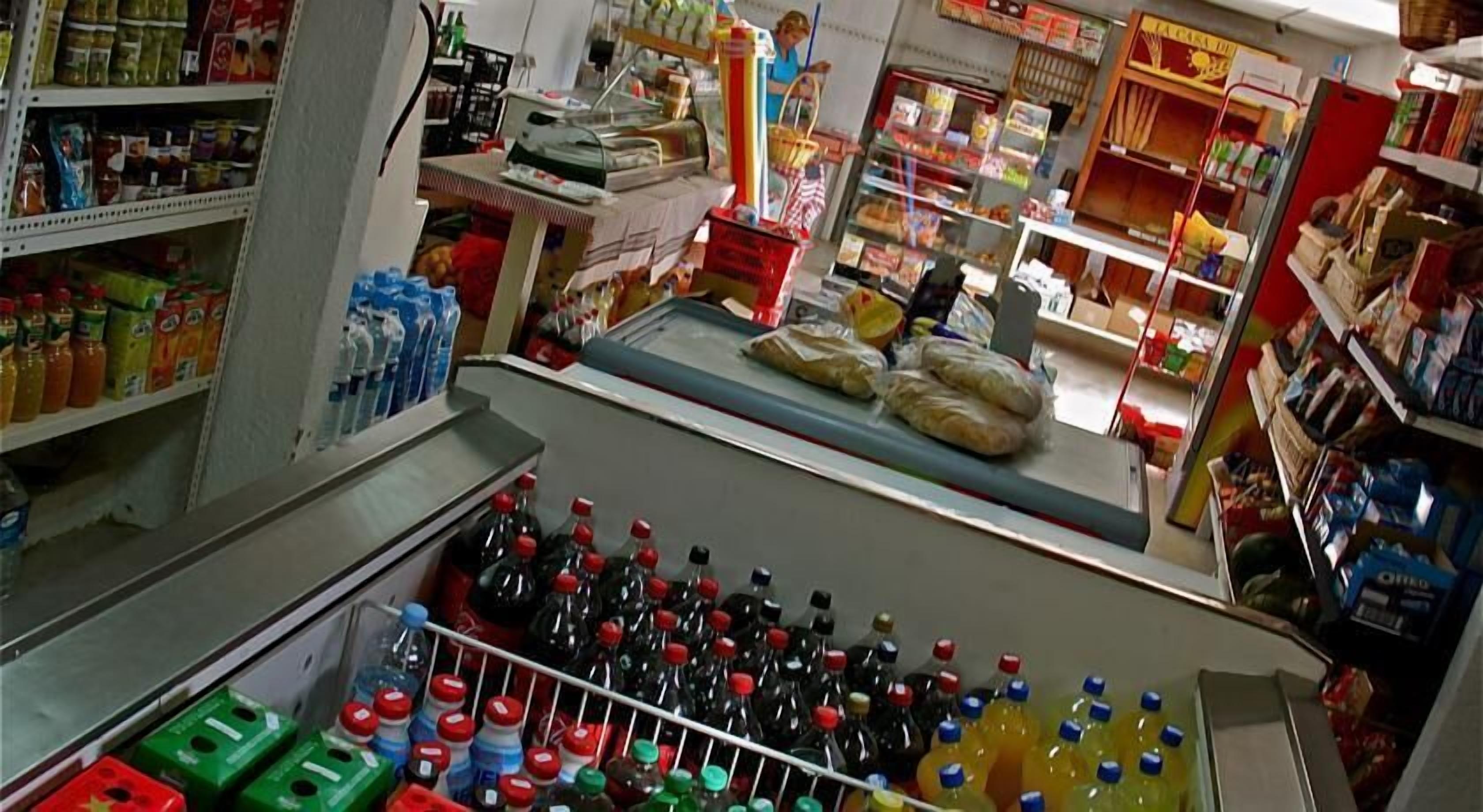 A grocery store with shelves stocked with various products, a checkout counter, and a person in the background.
