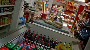 Een supermarkt met gevulde schappen, een kassa en een persoon op de achtergrond.